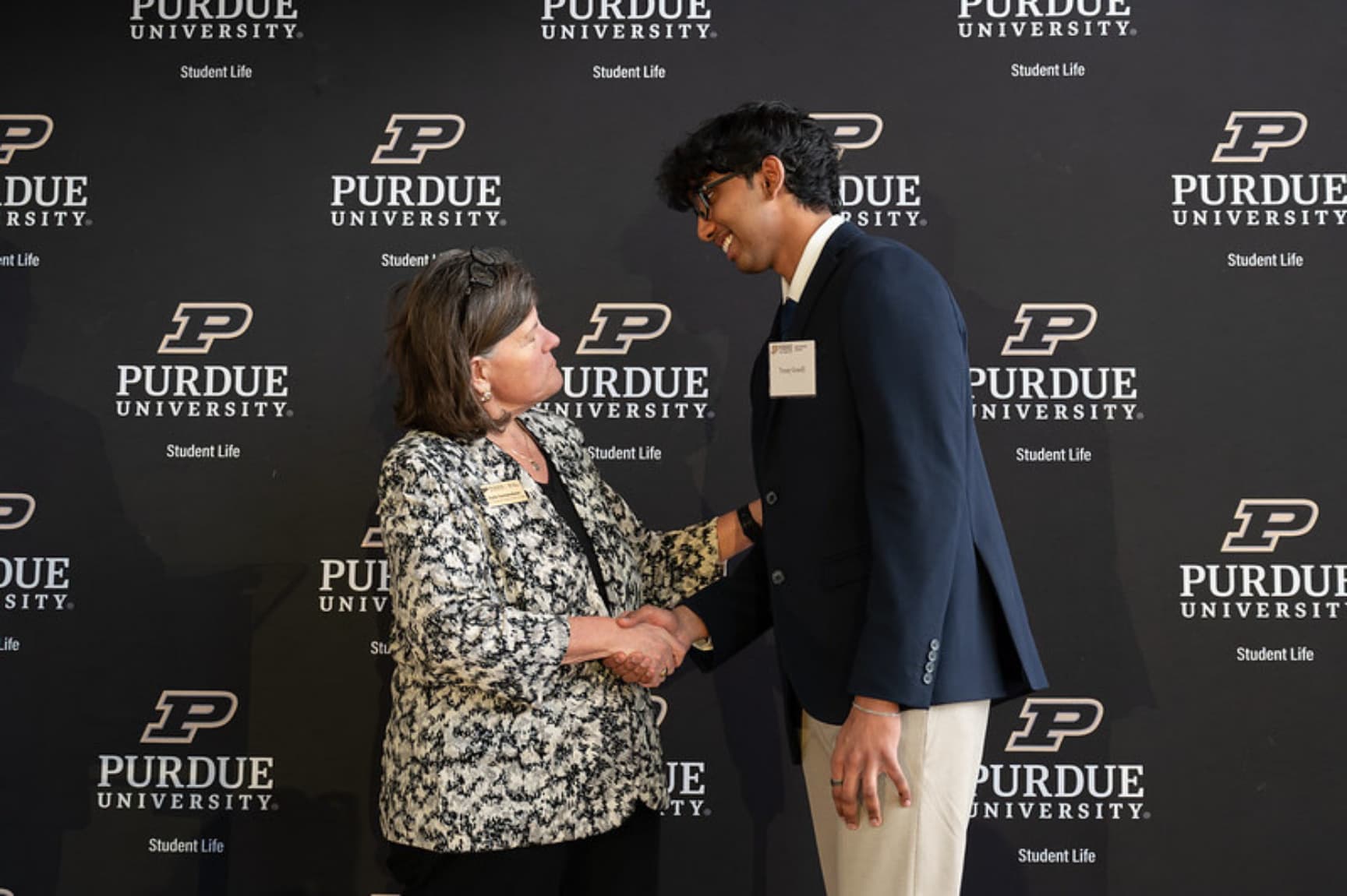 A Hack the Future member shaking hands with a Purdue Student Life representative in front of a Purdue University backdrop