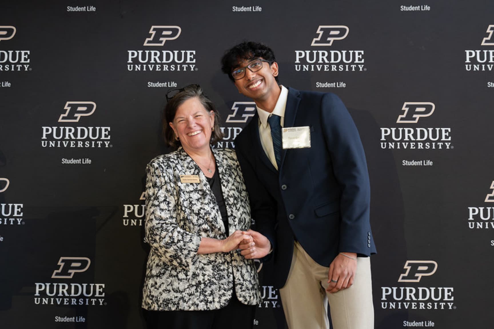 A Hack the Future member and a Purdue Student Life representative smiling together in front of a Purdue University backdrop